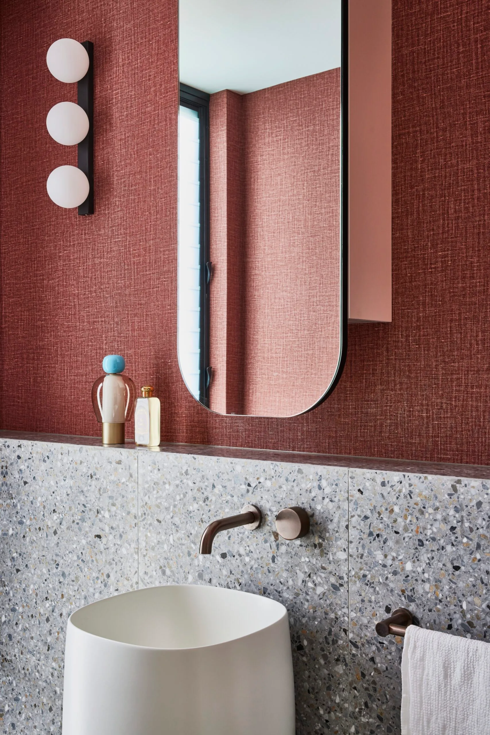 A powder room with red wallpaper above a tiled half wall with a freestanding basin.