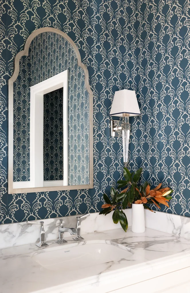 A powder room with blue patterned wallpaper, a marble vanity benchtop and a wall mirror.