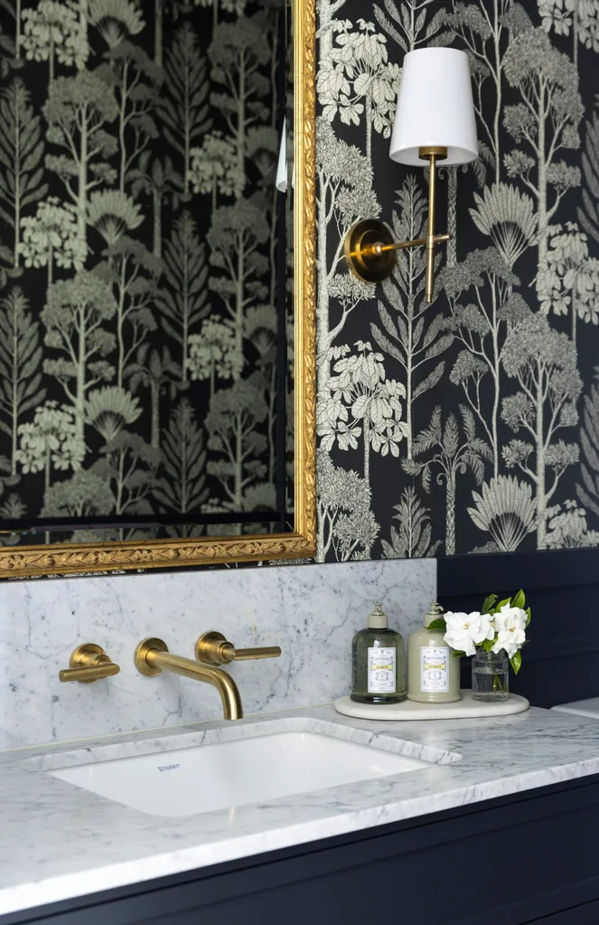 A powder room with a gold framed mirror, wall lights, marble benchtop and splashback and brass tapware.
