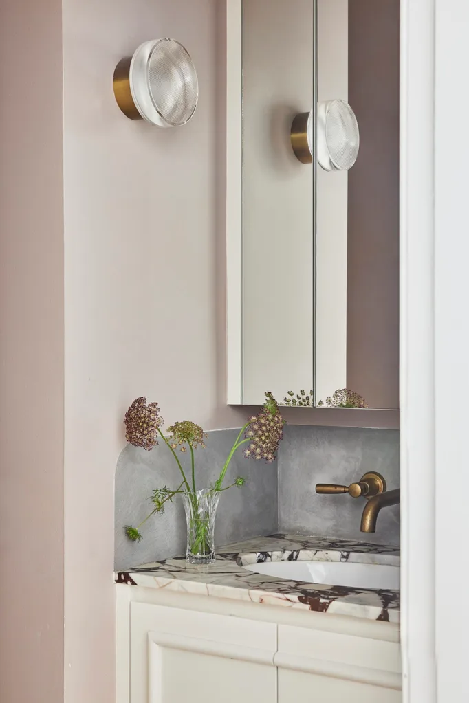 A powder room with a marble vanity benchtop, white cabinetry and brass tapware.