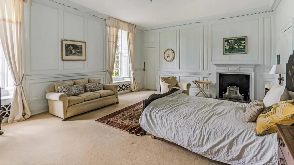 A bedroom with a fireplace, wainscoting and other decorative moulding on walls finished in a light blue shade.