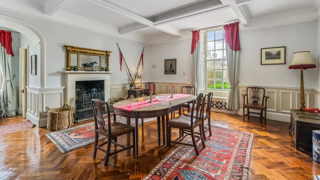 A dining room with traditional features such as coffered ceilings, wainscoting, a grand fireplace and timber dining table and chairs.