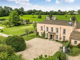 A grand stone manor house, built in 16th Century style with a Queen Anne front pillared portico. Grounds surround the home with trees, hedges, bushes and lush grass. This house was the filming location of the Bennet family house in the BBC adaptation of Jane Austen's Pride and Prejudice.
