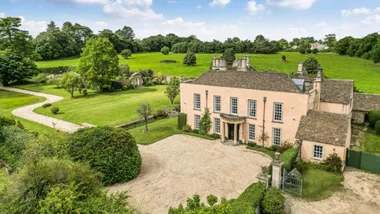 A grand stone manor house, built in 16th Century style with a Queen Anne front pillared portico. Grounds surround the home with trees, hedges, bushes and lush grass. This house was the filming location of the Bennet family house in the BBC adaptation of Jane Austen's Pride and Prejudice.