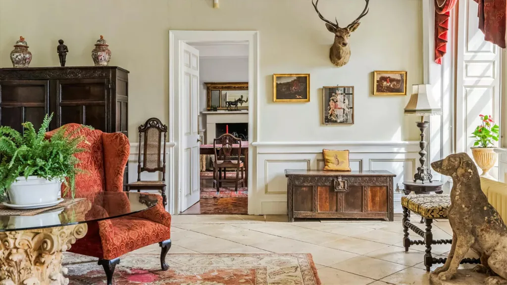 A tiled room with a wingback armchair, tiled flooring, walls with wainscoting and art in golden frames with a deer head positioned above.