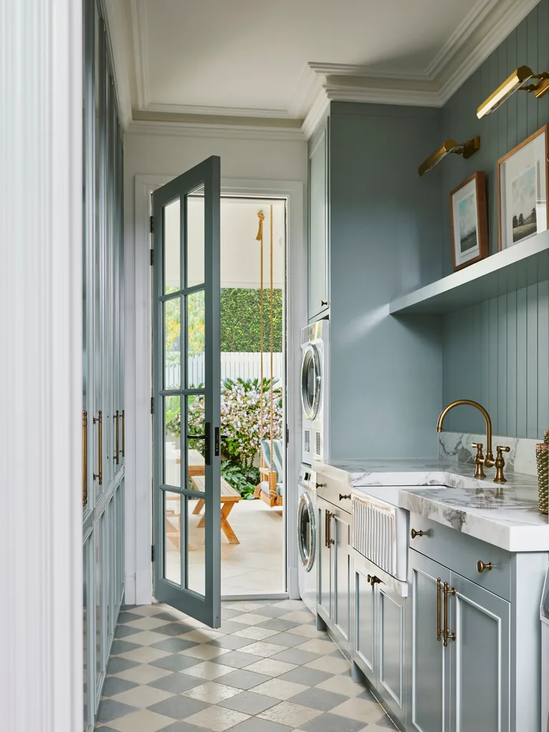Laundry room with blue joinery, marble countertop, brass tapware and hardware, checkered floor, open door leading to an alfresco dining area and garden.