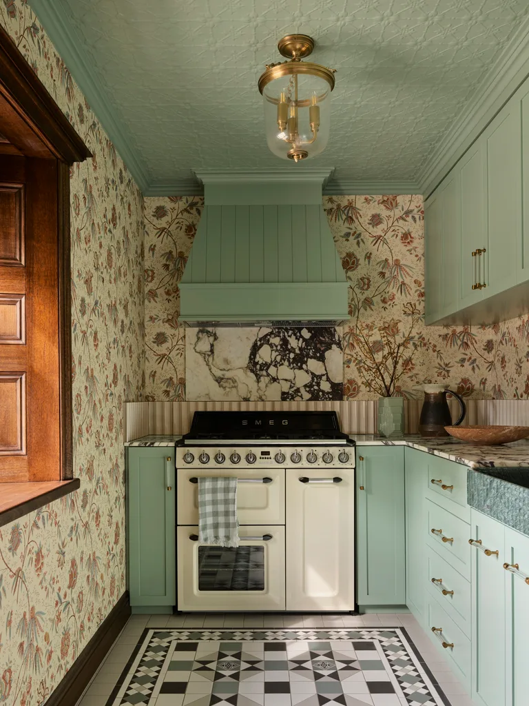 Mint green kitchen with vintage oven, patterned wallpaper, marble splashback and geometric floor tiles. The ceiling, cabinetry and rangehood are all finished in mint green.
