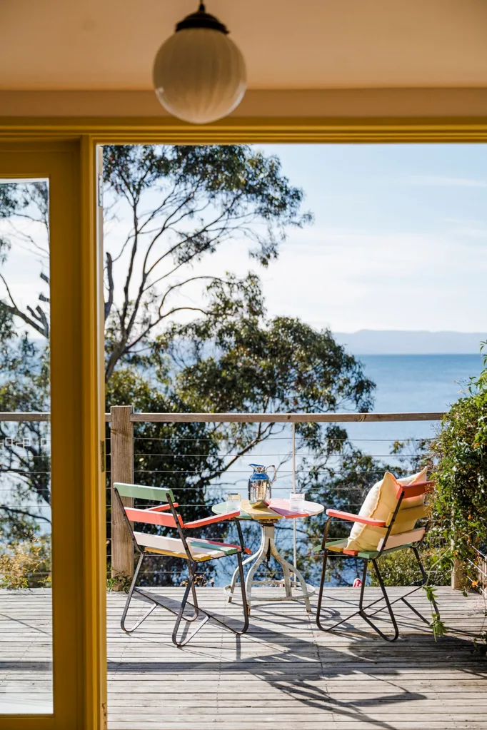 The back deck in this Tasmanian Airbnb has wide, sweeping views of the surrounding bay. A small, round outdoor table and two chairs are positioned on the deck.