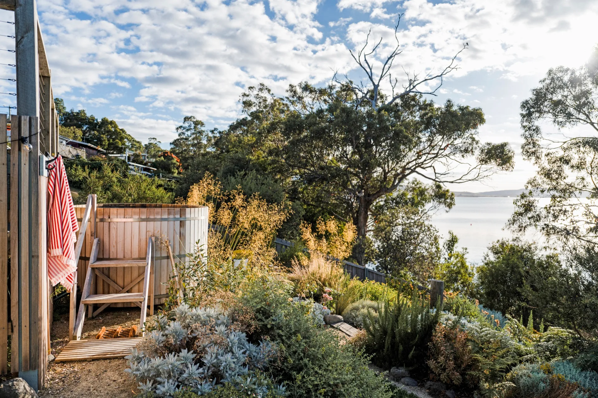 The backyard of this Tasmanian Airbnb has sea views, with a hot tub set up to maximise those views. Plants and trees decorate the area around the hot tub.