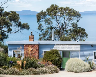 This fishing shack has been renovated into a colourful and pattern-filled Airbnb in Tasmania. The blue panelled exterior matches the blue of the sea views visible beyond the house. colourful coastal homes.