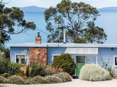This fishing shack has been renovated into a colourful and pattern-filled Airbnb in Tasmania. The blue panelled exterior matches the blue of the sea views visible beyond the house. colourful coastal homes.