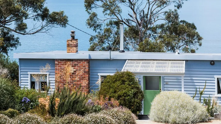 This fishing shack has been renovated into a colourful and pattern-filled Airbnb in Tasmania. The blue panelled exterior matches the blue of the sea views visible beyond the house. colourful coastal homes.