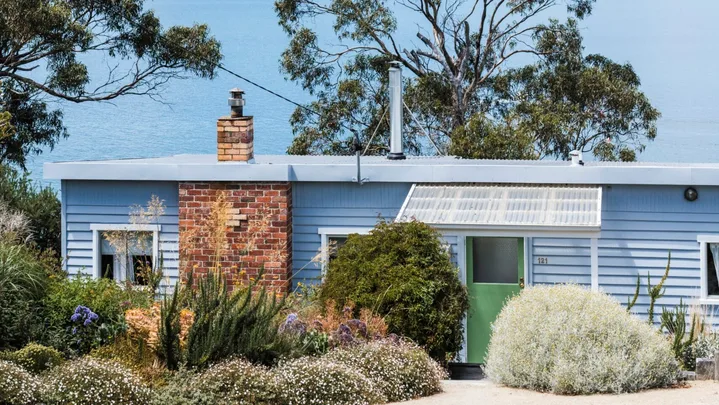 This fishing shack has been renovated into a colourful and pattern-filled Airbnb in Tasmania. The blue panelled exterior matches the blue of the sea views visible beyond the house.