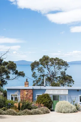 This fishing shack has been renovated into a colourful and pattern-filled Airbnb in Tasmania. The blue panelled exterior matches the blue of the sea views visible beyond the house.