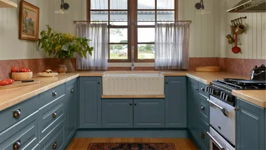 A kitchen with blue cupboards and a kitchen rug