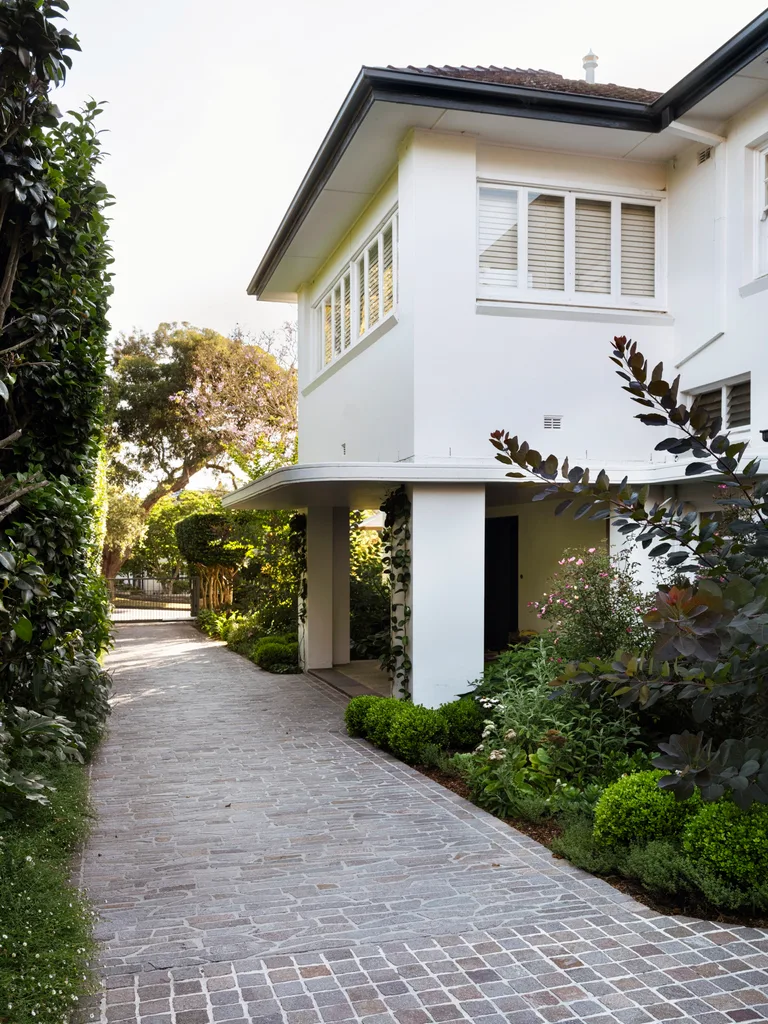 Softened by layered plantings of lush foliage, the entry portico with its Art Deco curved canopy forms a strong first impression. Ivy graces two pillars.