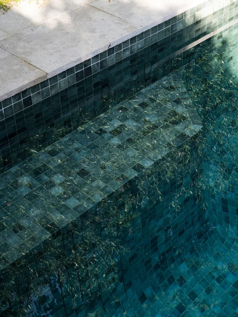 A close up photo of a pool with square tiles. The water in the pool often reflects the ivy that covers the wall next to it.