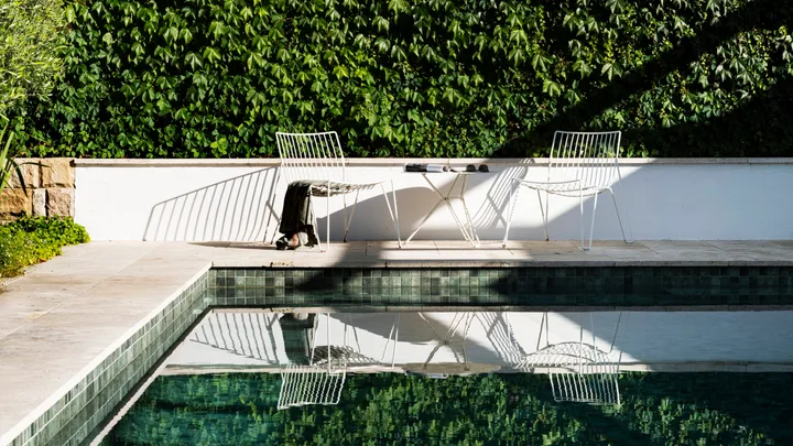A rectangular swimming pool, surrounded by large stone pavers with a wall covered in Boston ivy in the background.