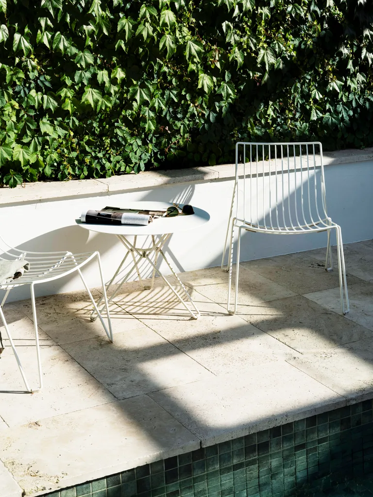 Boston ivy disguises the garage wall behind the swimming pool. Two white wire chairs are positioned by the pool, with a round white table in the middle.