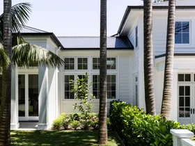 Large white house with palm trees and lush green lawn in sunny garden setting.