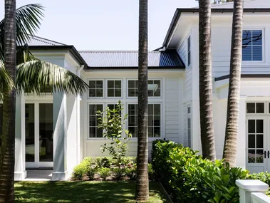 Large white house with palm trees and lush green lawn in sunny garden setting.