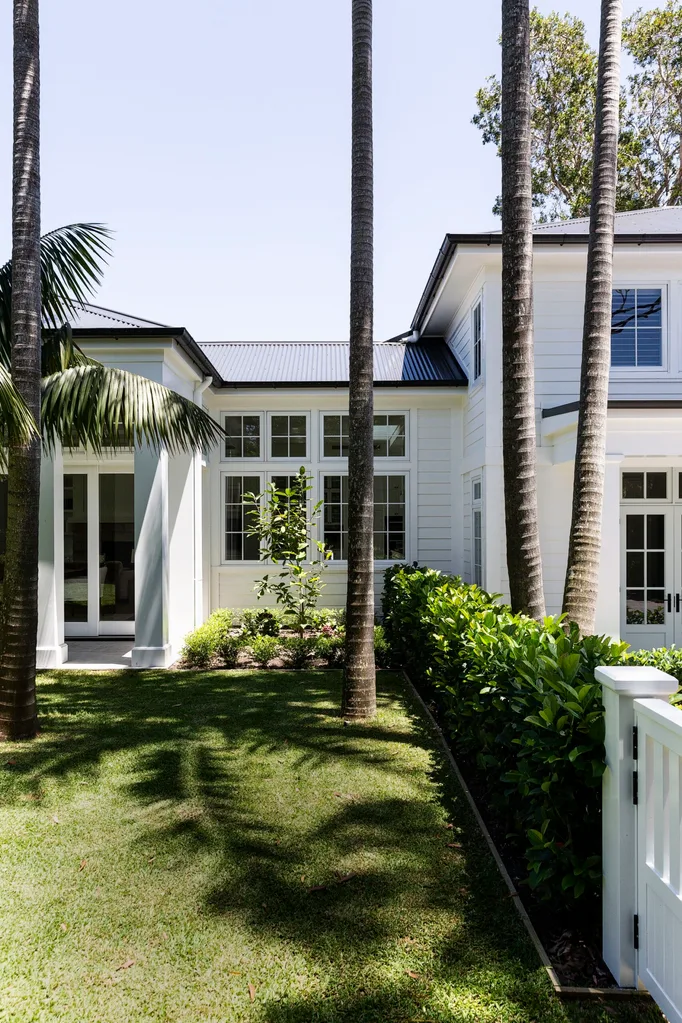 Large white house with palm trees and lush green lawn in sunny garden setting.