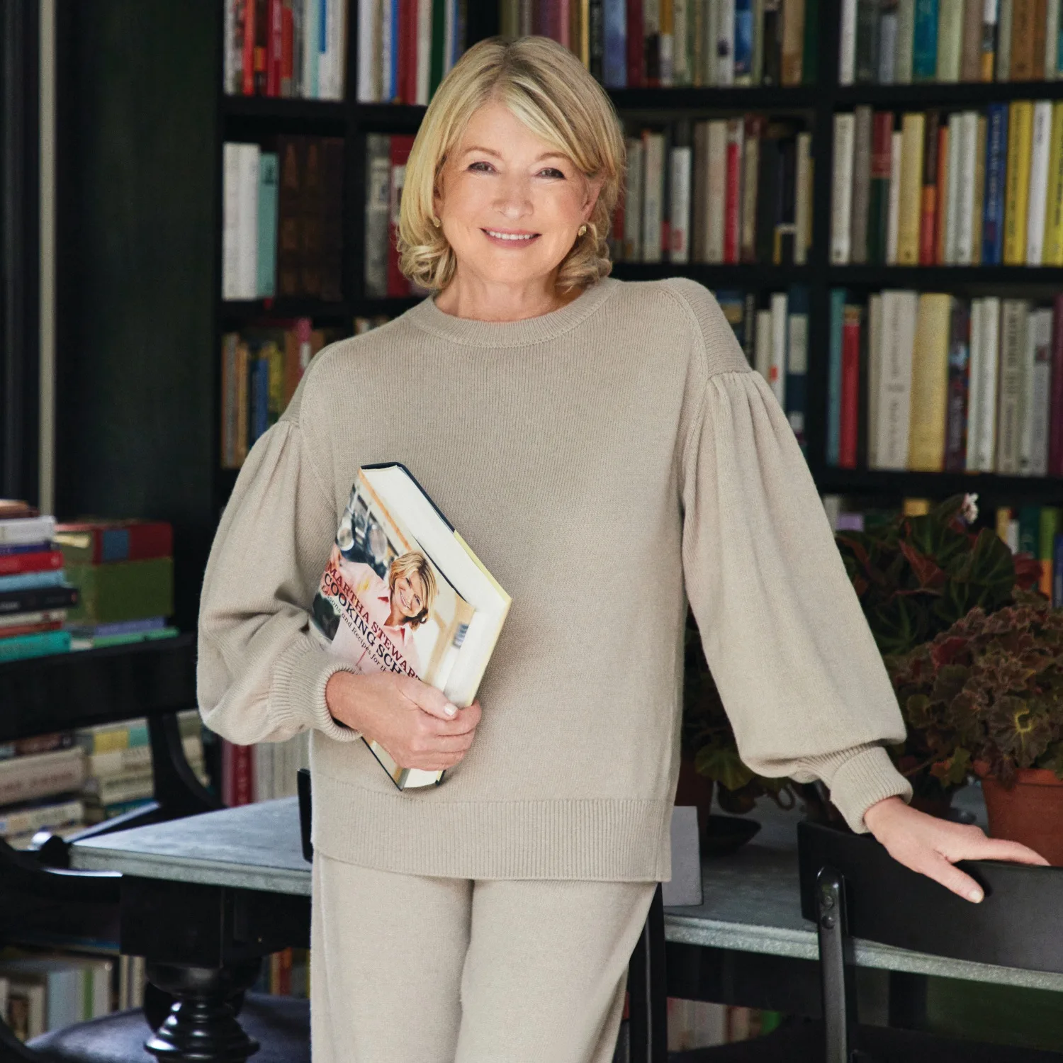 Martha Stewart holding a book next to a bookshelf