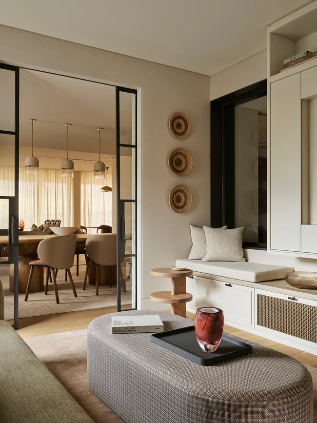 Modern living room with neutral tones, featuring a cozy seating area, decorative wall baskets, and a view into a dining room.