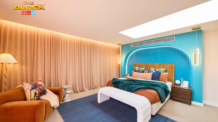A modern bedroom from "The Block" with a teal accent wall, velvet sofa, and ample lighting.