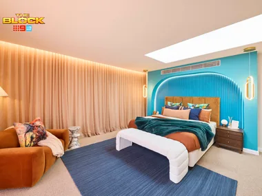 A modern bedroom from "The Block" with a teal accent wall, velvet sofa, and ample lighting.