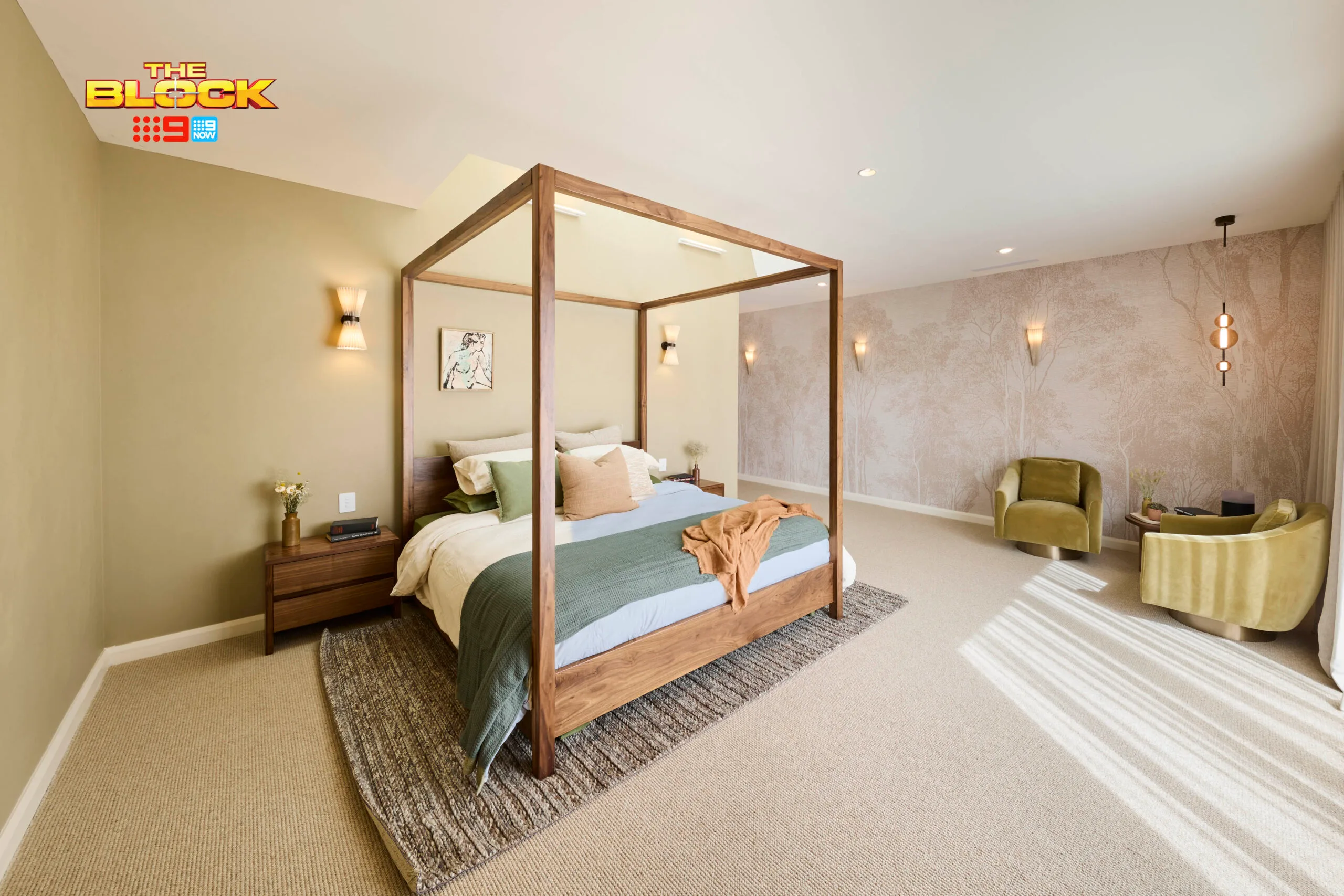 Modern bedroom with a canopy bed, neutral tones, wall artwork, carpet, and green chairs, from "The Block" show.