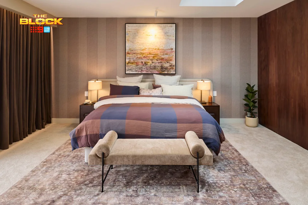 Stylish bedroom from "The Block" with striped bedding, art, and lamps, featuring a beige bench at the foot of the bed.