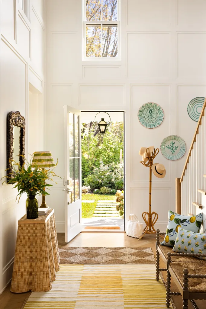 Bright entryway with open door, woven decor, hanging hats, and greenery visible outside.