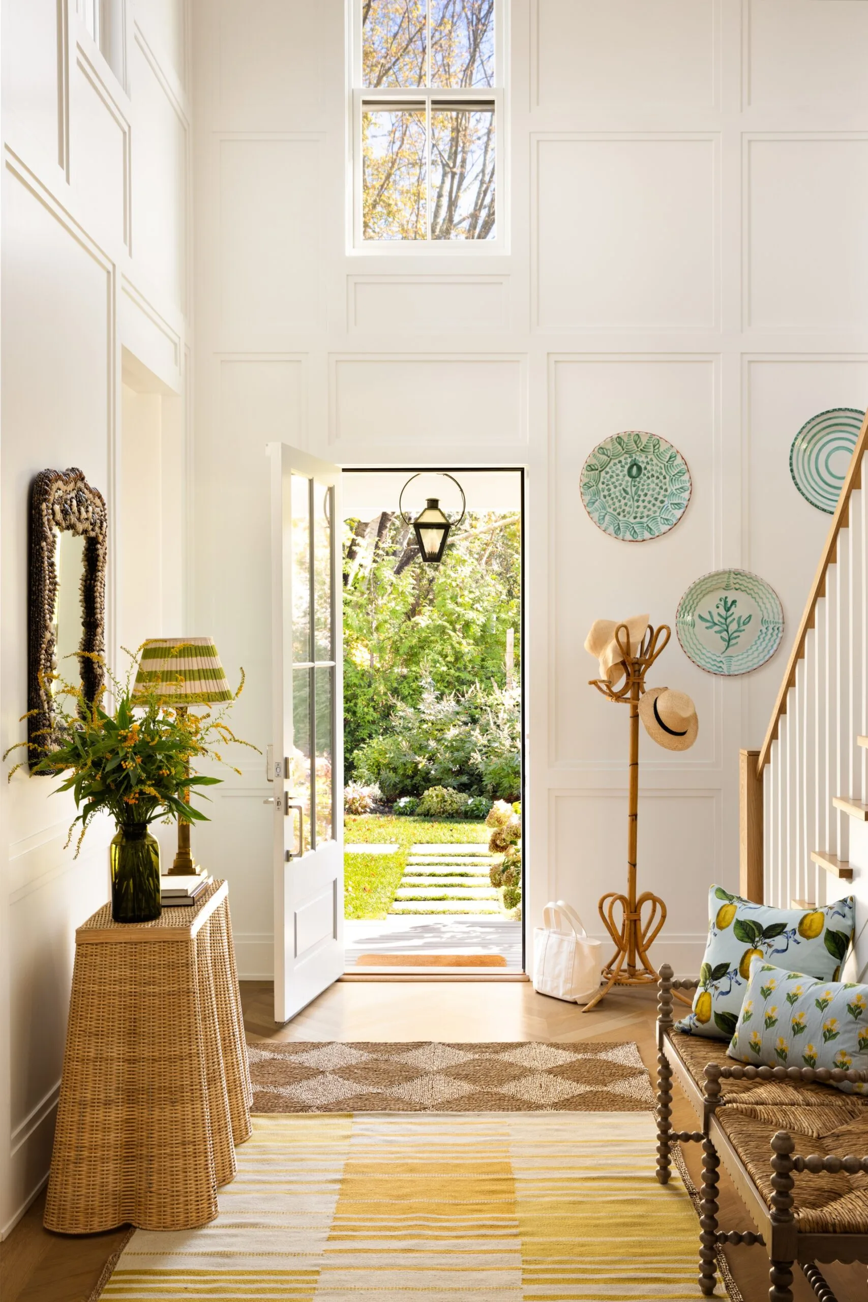 Bright entryway with open door, woven decor, hanging hats, and greenery visible outside.