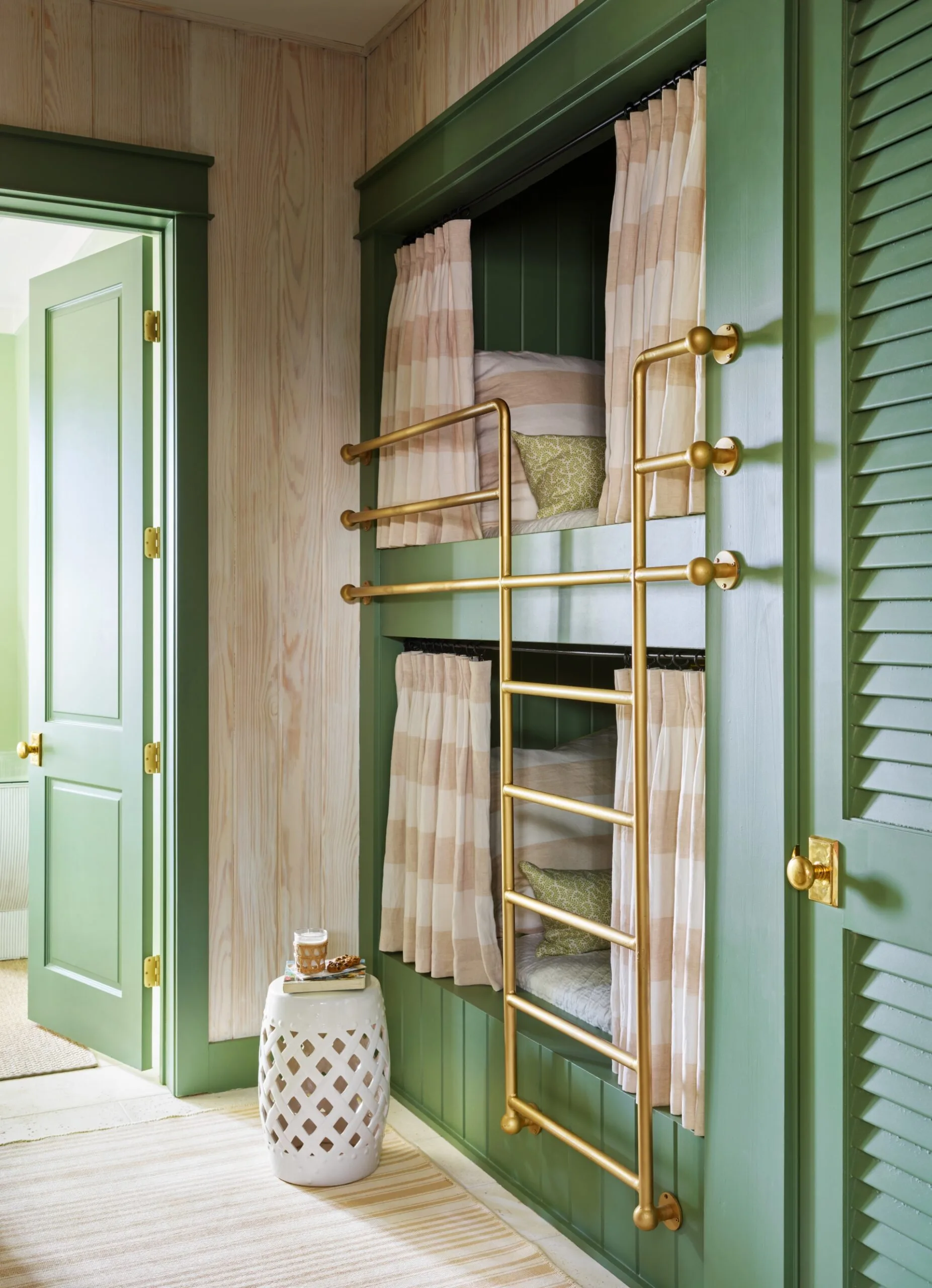 Built-in green bunk beds with gold railings and striped curtains, next to a small white side table with a drink.