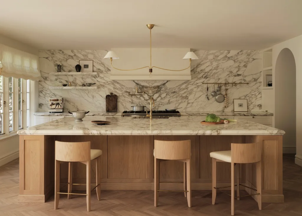 Elegant kitchen with marble countertops, wooden stools, a hanging light fixture, and potted plants on the counter.