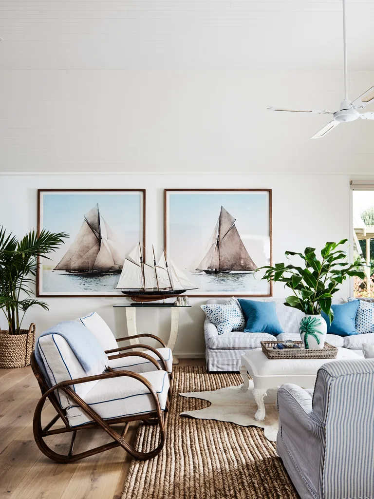 Coastal-themed living room with sailboat art, rattan chairs, and blue cushions. Living room ideas.