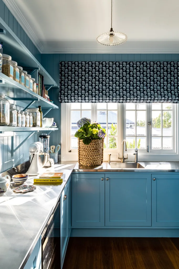 Cozy blue pantry with open shelves, natural light, and a woven basket plant on the counter by the window.