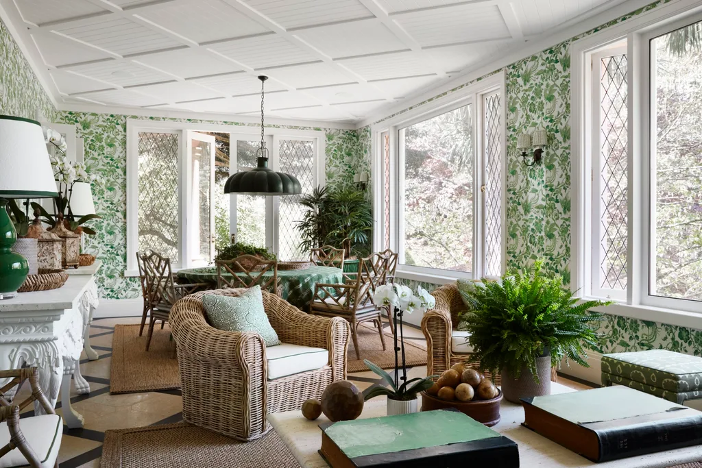Sunroom with wicker chairs, green floral wallpaper, and large windows offering natural light and outdoor views.