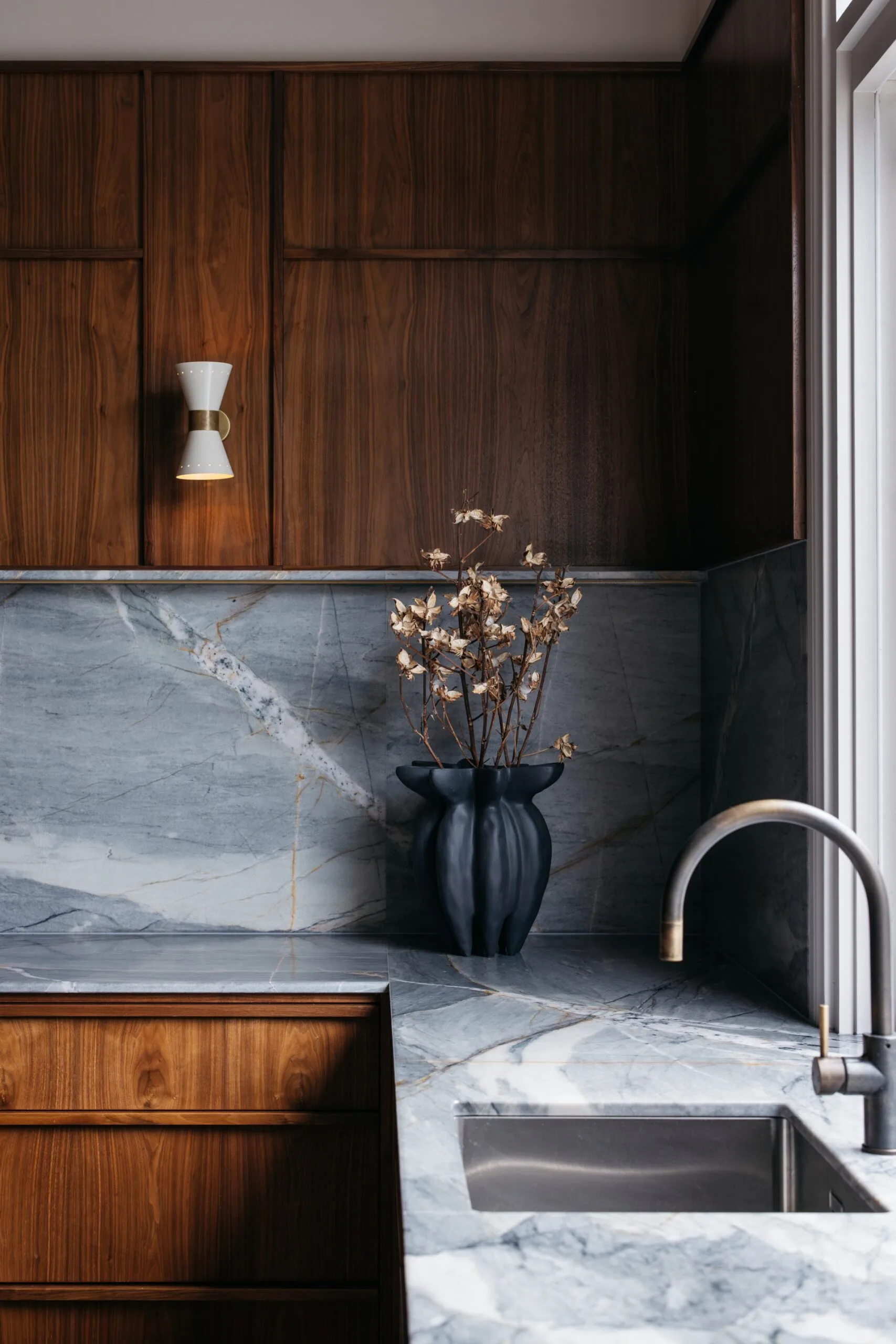 Close-up detail of American walnut kitchen with quartzite stone splashback and benchtop. A ceramic vessel sits on the benchtop.