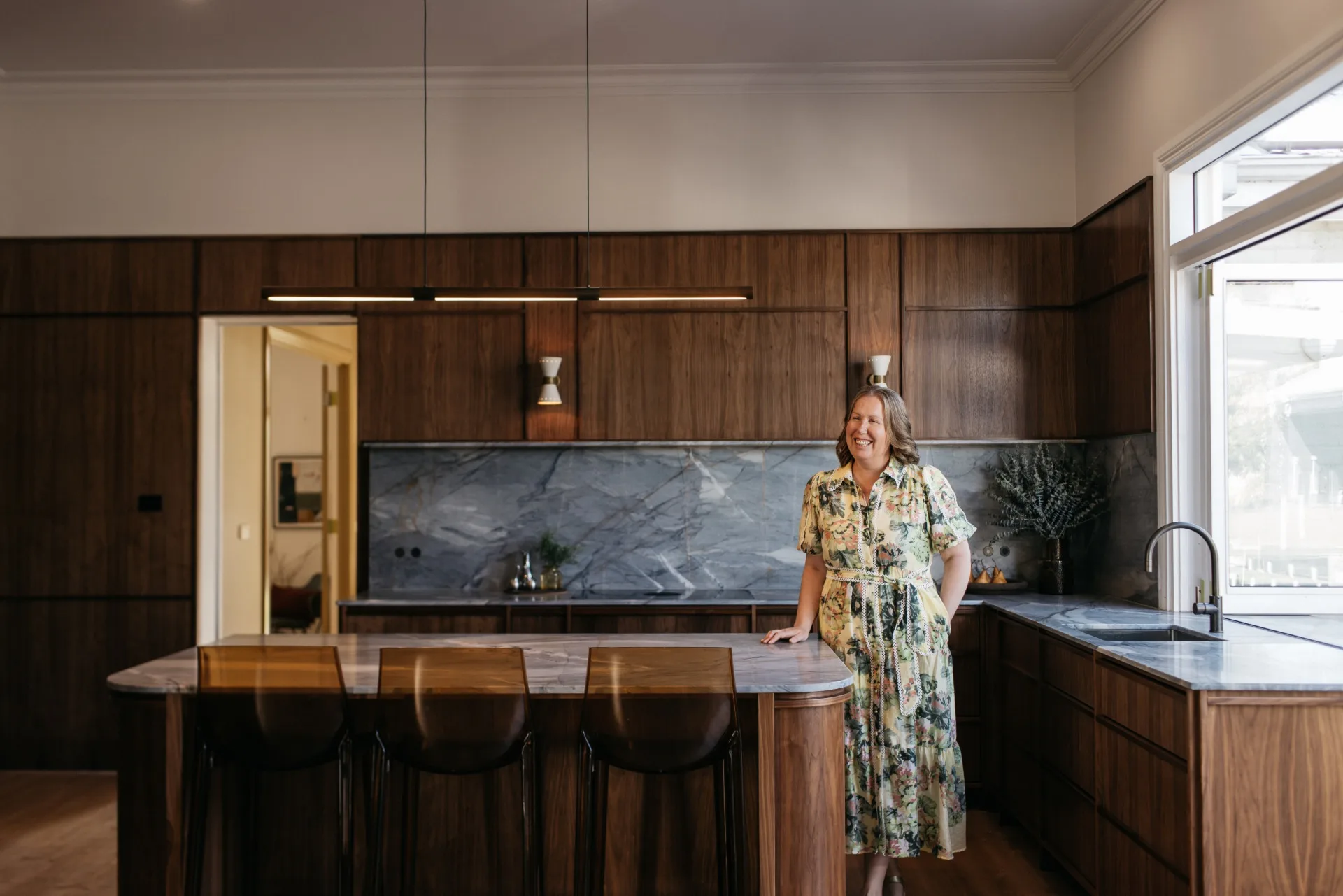 Interior designer Carlie Fraser of Hygge Design in her American walnut kitchen with quartzite stone splashback and benchtop, and ghost bar stools.