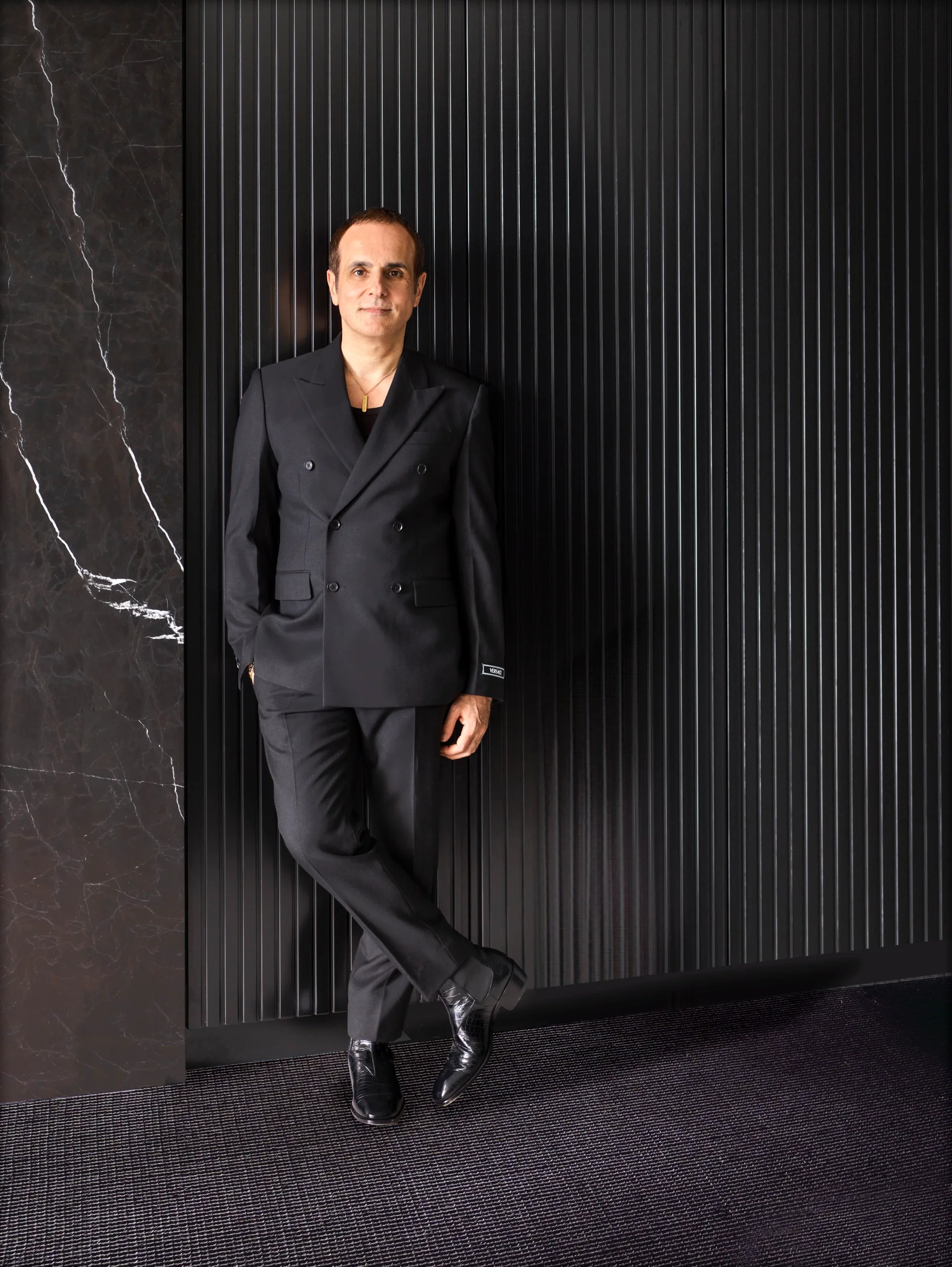 Australian design influencer Greg Natale in a black suit, in front of a black wall.