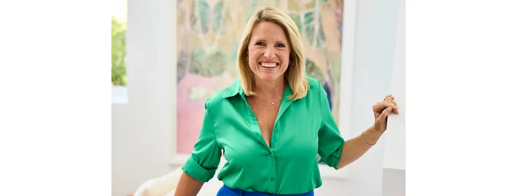 Australian design influencerf Wendy Moore smiles in a green blouse in a white interior with a piece of artwork behind her.