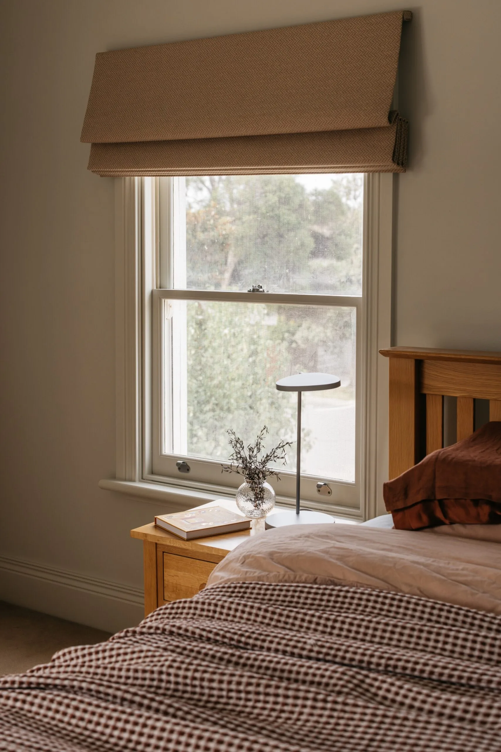 Bedroom with a neutral, warm palette and Roman blinds on traditional sash windows.