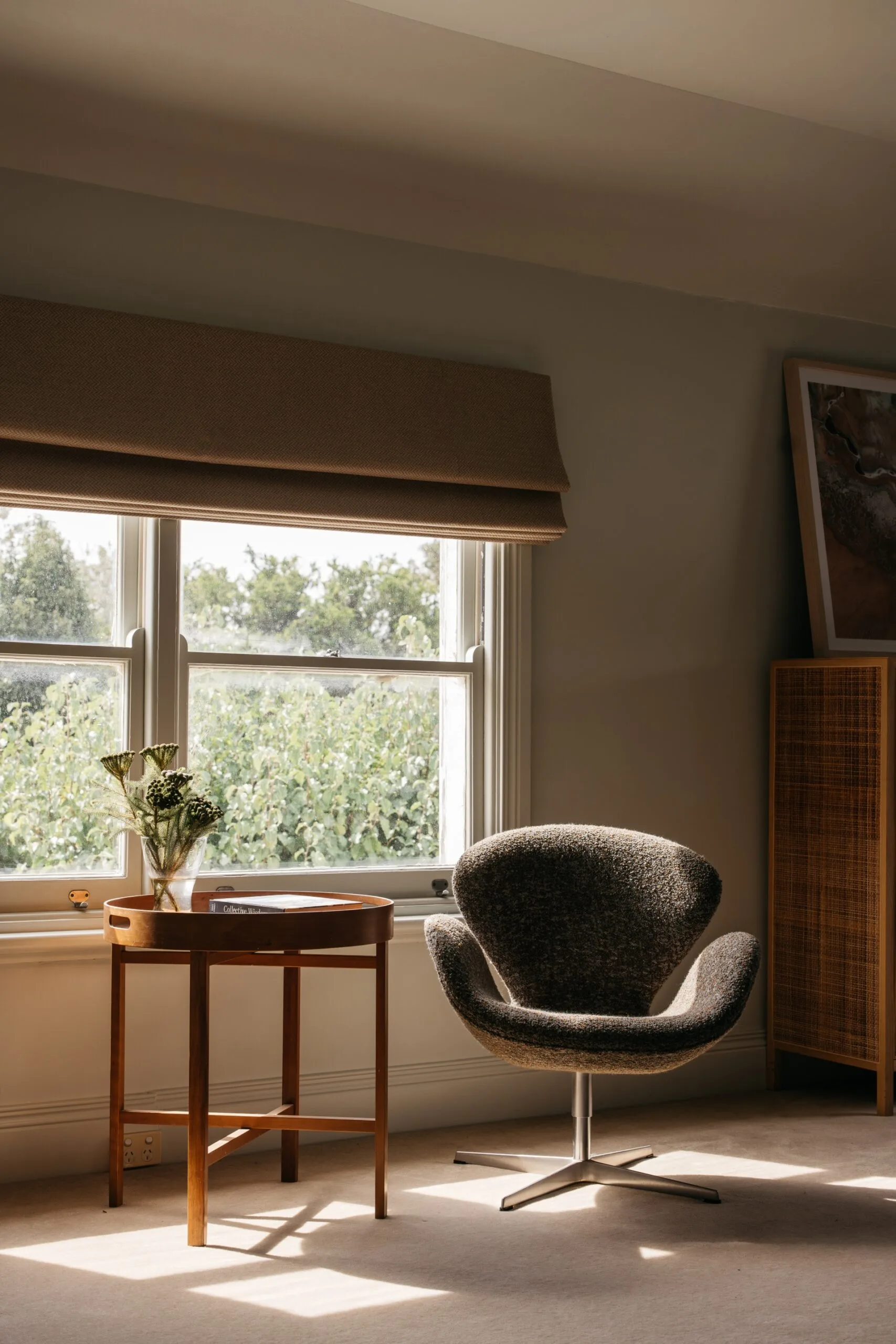 Bedroom including a midcentury-style occasional chair and side table by a window with Roman blinds.