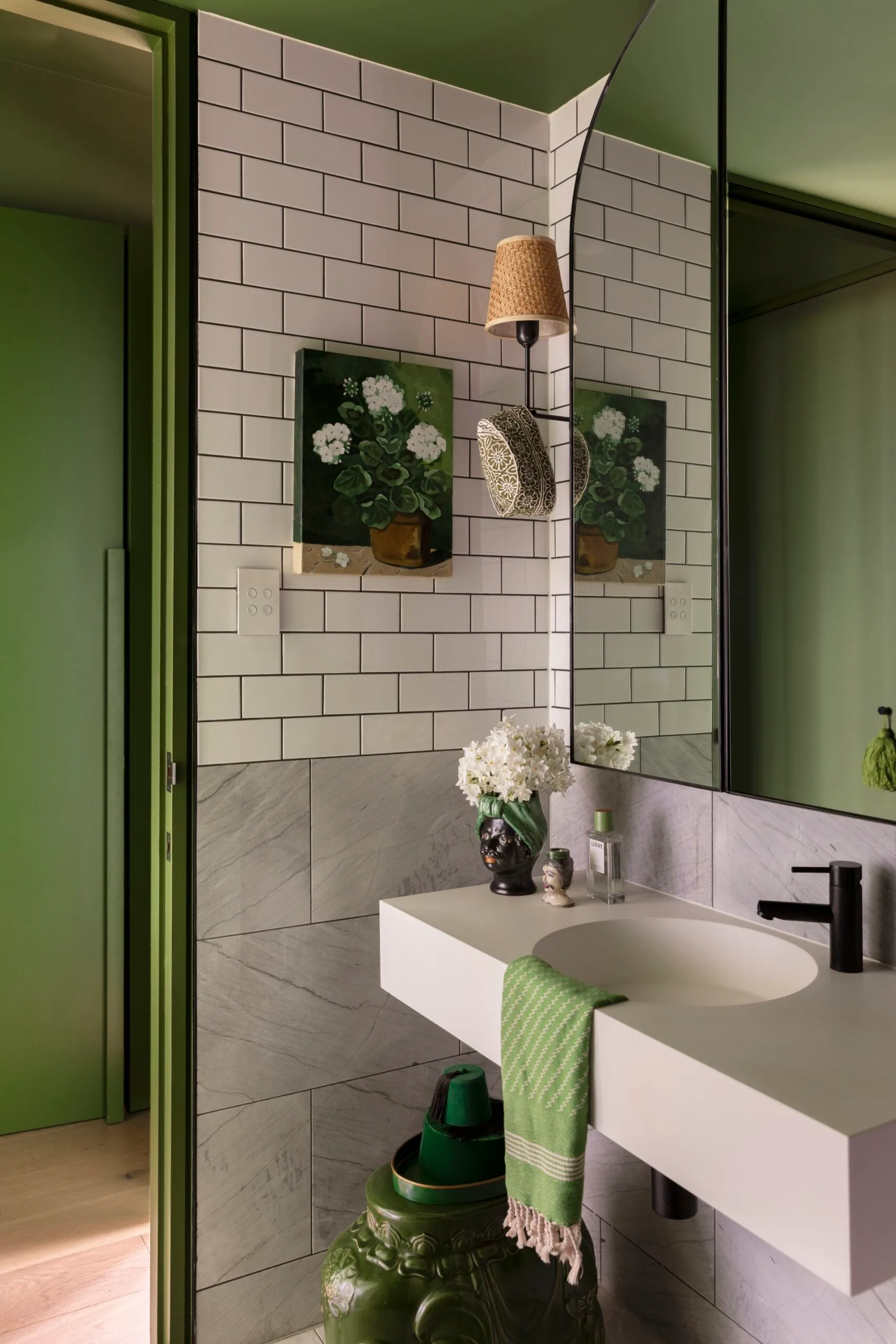 Modern bathroom with green accents, white subway tiles, floating sink, and potted plants.