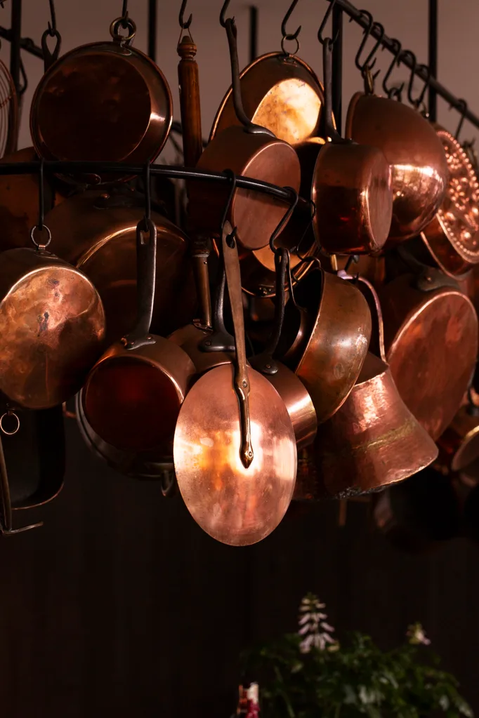 Hanging copper pots and pans on a rack against a dark background.
