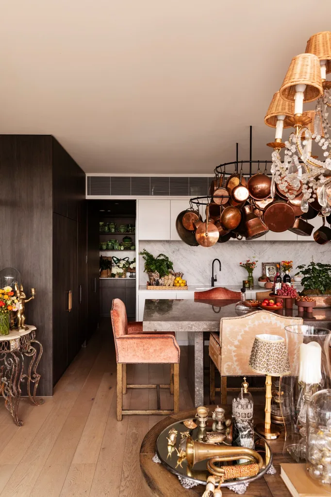 Luxurious kitchen with a large marble island, hanging copper pots, elegant decor, and plush chairs. This is the kitchen of TV star Chyka Keebaugh.