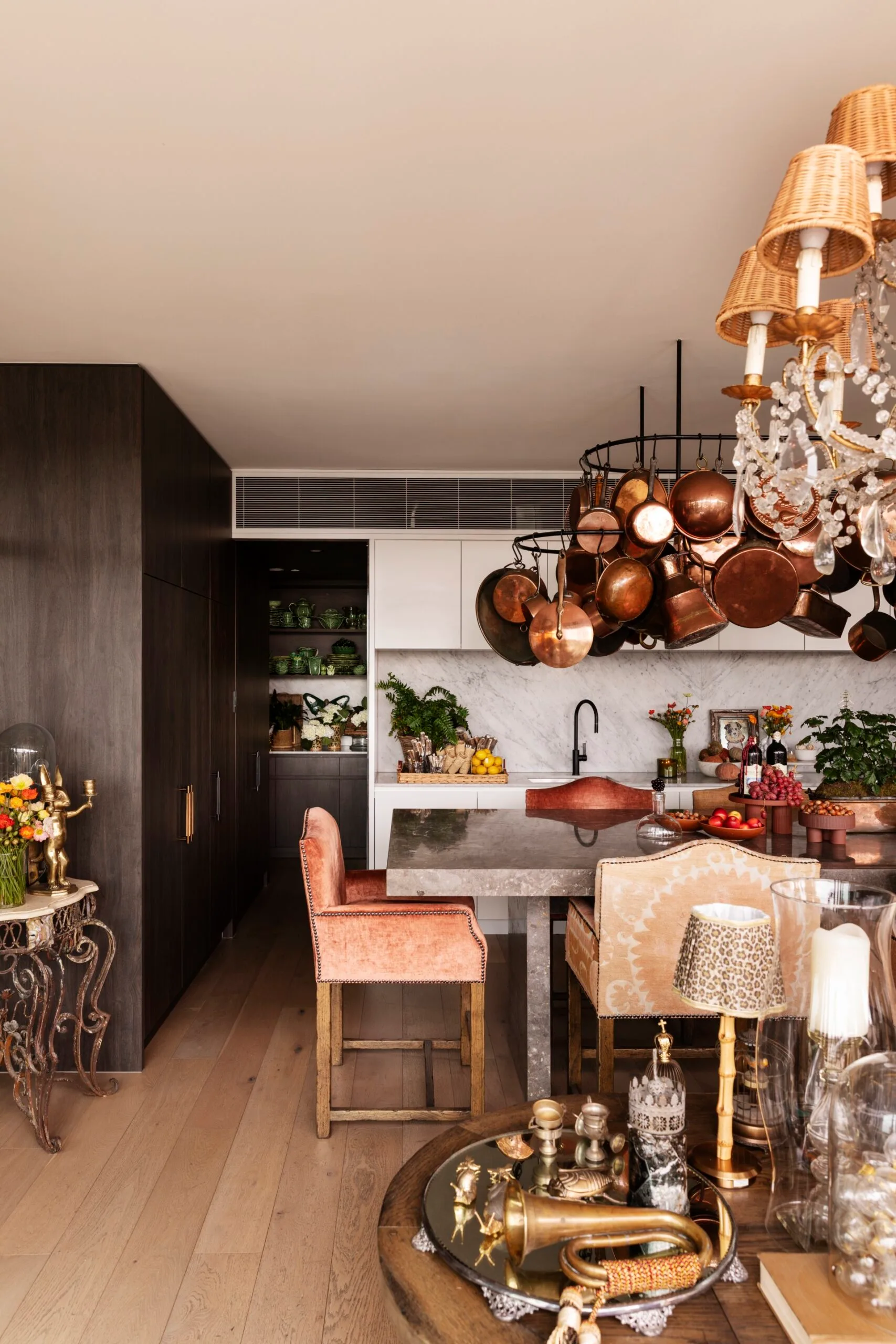 Luxurious kitchen with a large marble island, hanging copper pots, elegant decor, and plush chairs. This is the kitchen of TV star Chyka Keebaugh.