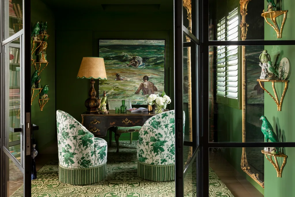 Elegant green room with floral chairs, painting, ornate desk, gold shelves with parrots, and a warm lamp. This is the library of TV star Chyka Keebaugh.